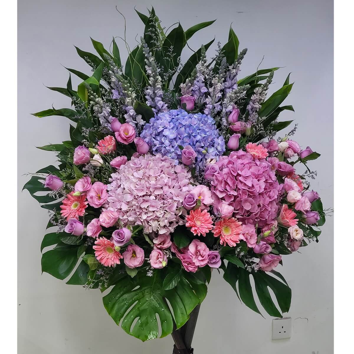 Large standing arrangement featuring pink, lilac, and blue hydrangeas, pink gerberas, lavender and blush roses, pink lisianthus, and light purple snapdragons - 大型花牌設計，以粉紅、淡紫與藍色繡球花、粉非洲菊、紫及粉玫瑰、粉洋桔梗與淡紫金魚草組成