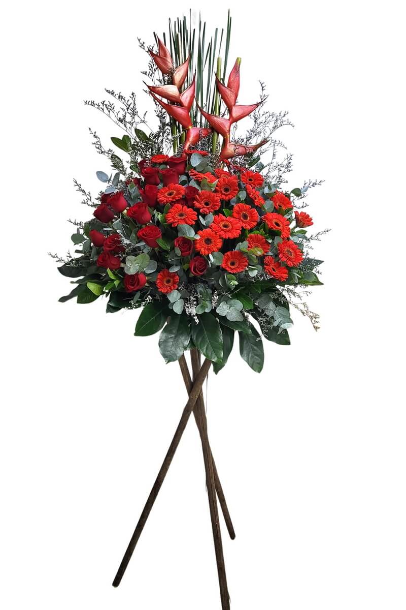 Standing flower arrangement with red roses, red gerberas, heliconias, eucalyptus, and greenery on wooden tripod - 紅玫瑰、紅扶郎、赫蕉、尤加利及綠葉三腳木架花牌