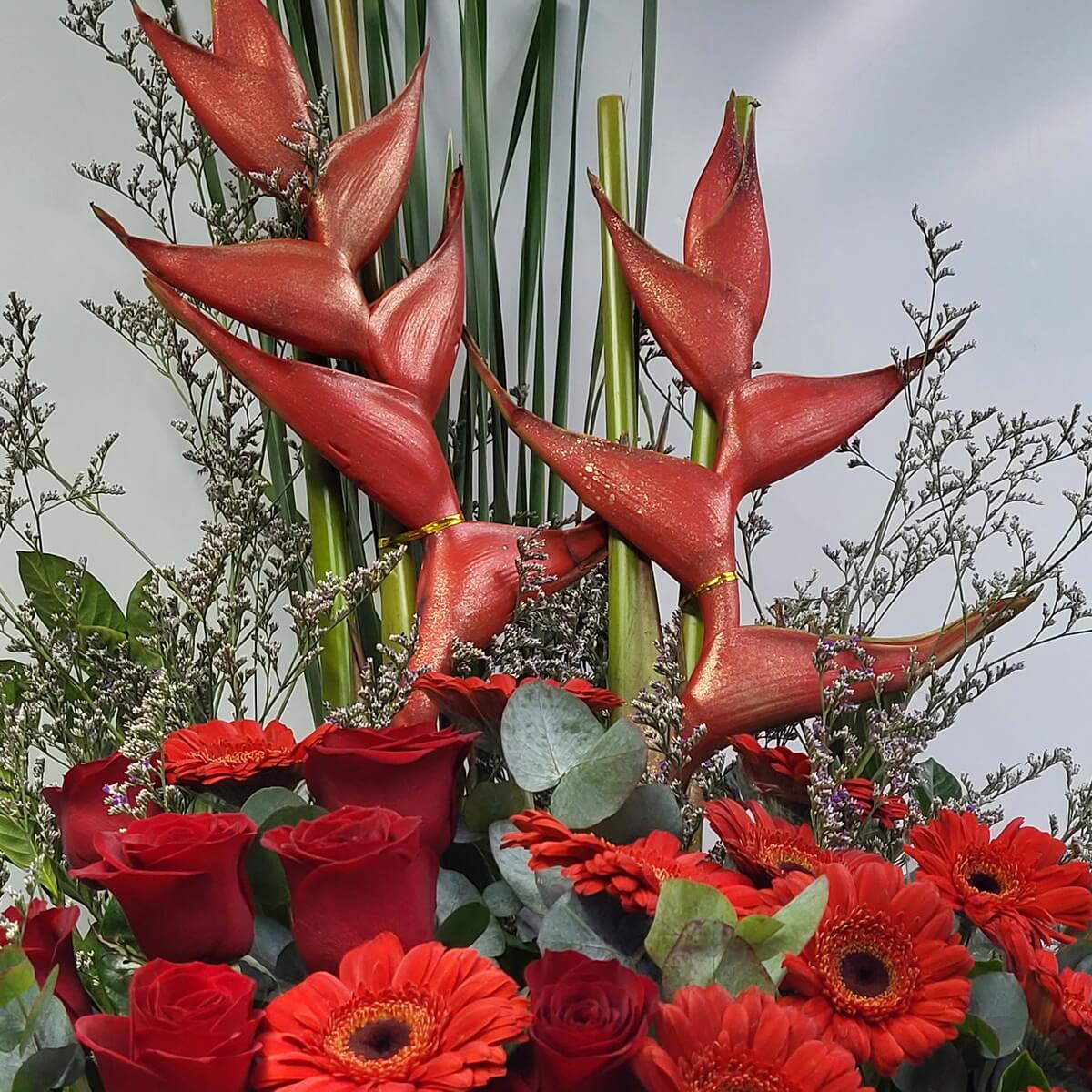 Close-up of glossy red heliconias with metallic sheen, arranged above red roses and gerberas, accented with eucalyptus leaves and fine filler branches - 帶金屬光澤紅赫蕉特寫，配紅玫瑰與紅扶郎，搭配尤加利與細緻襯枝