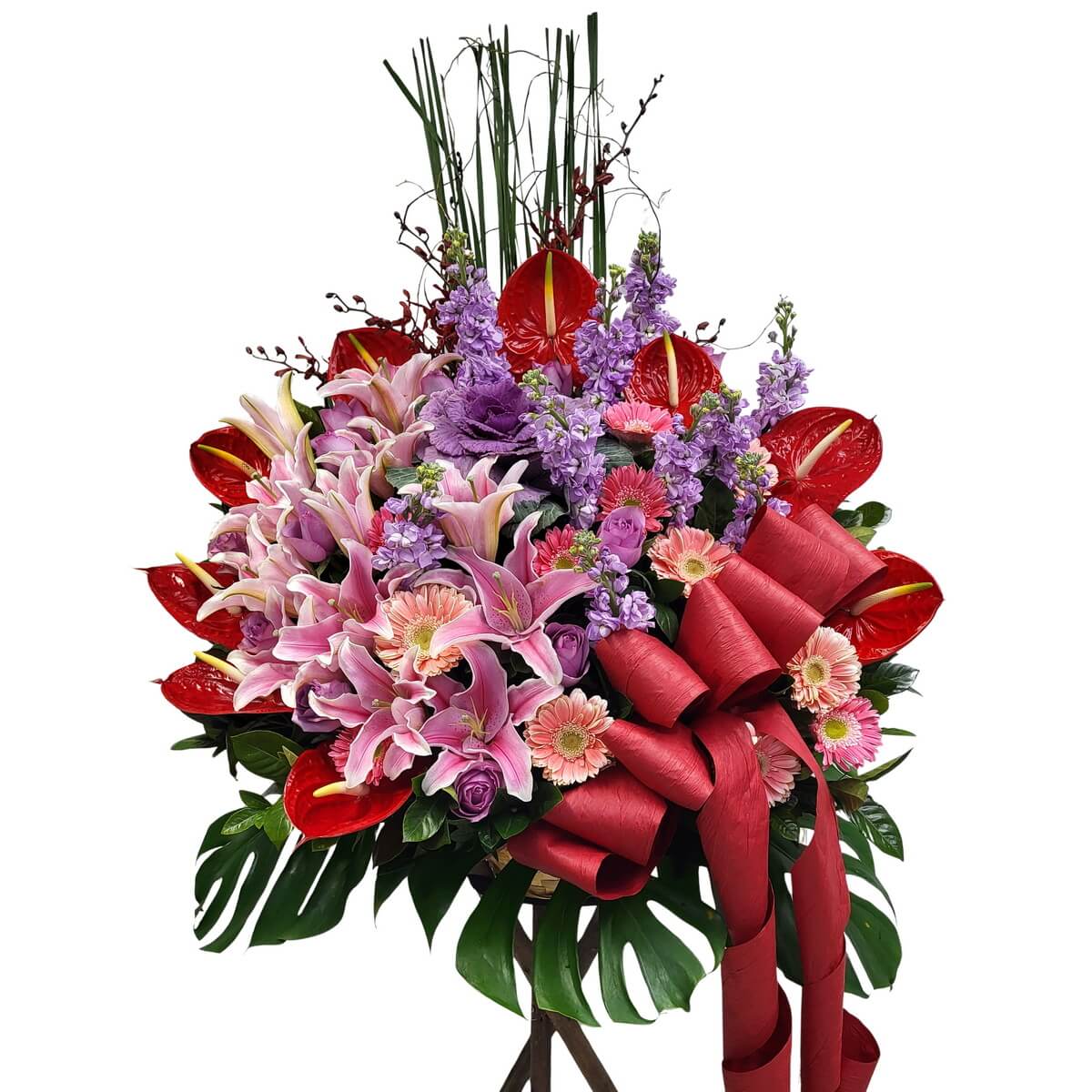 Floral stand featuring pink lilies, purple lisianthus, red anthuriums, peach gerberas, and lush greenery with red ribbon - 粉百合、紫洋桔梗、紅掌與蜜桃扶郎花牌，配綠葉及紅絲帶