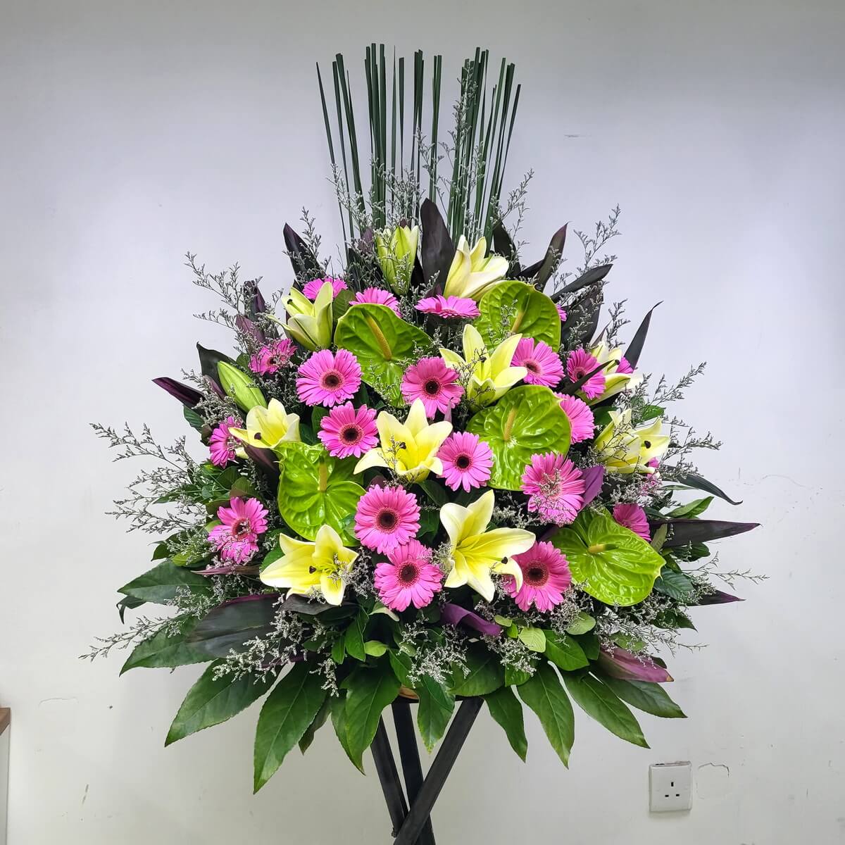 A vibrant grand opening stand with hot pink gerberas, soft yellow lilies, and glossy green anthuriums. 鮮豔粉紅太陽花搭配黃百合與青綠火鶴花，洋溢熱情活力，營造喜慶氛圍。
