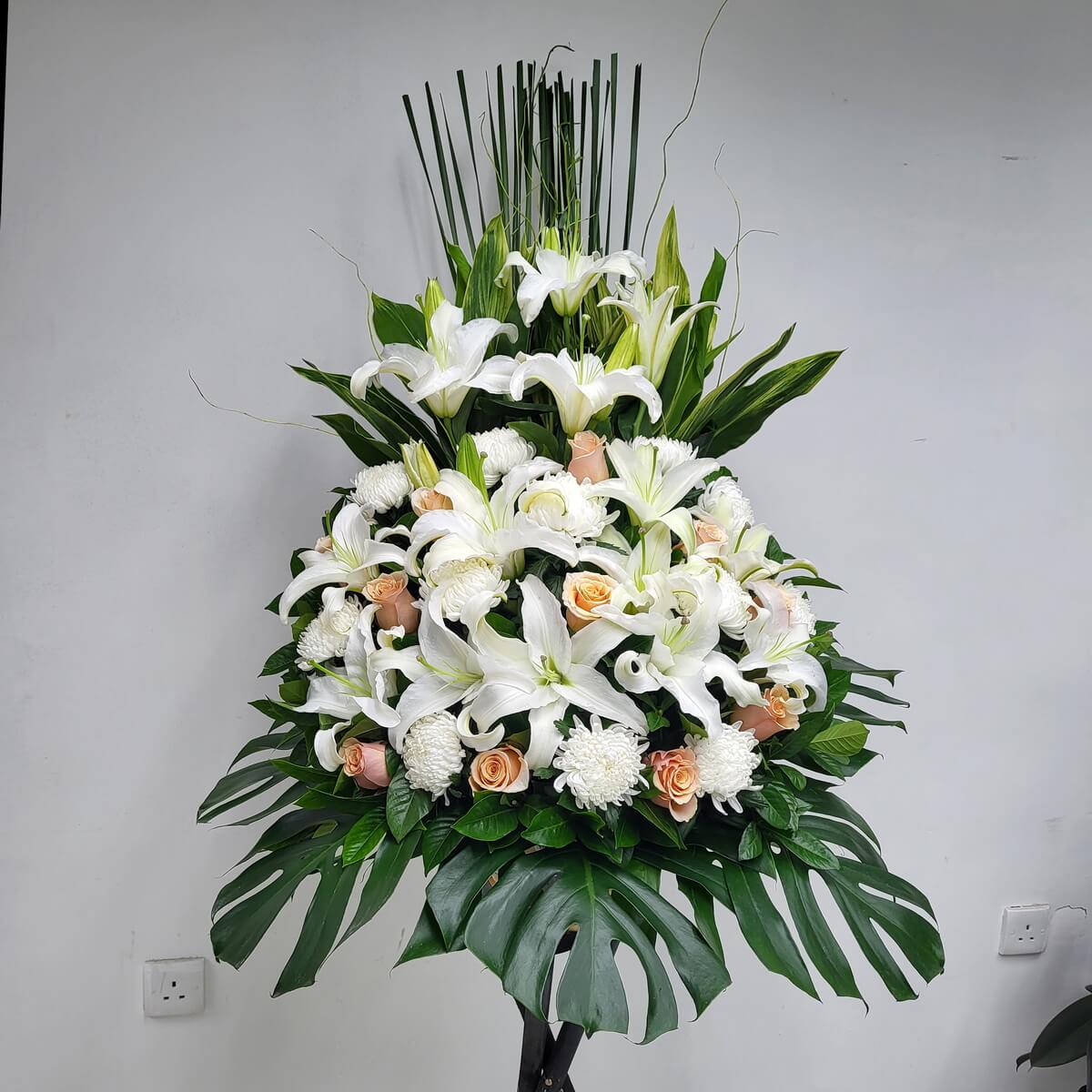 Graceful condolence arrangement of white lilies, soft peach roses, and chrysanthemums for heartfelt tribute.
優雅的白百合與蜜桃玫瑰、白菊悼念花牌，寄託深切追思與懷念。