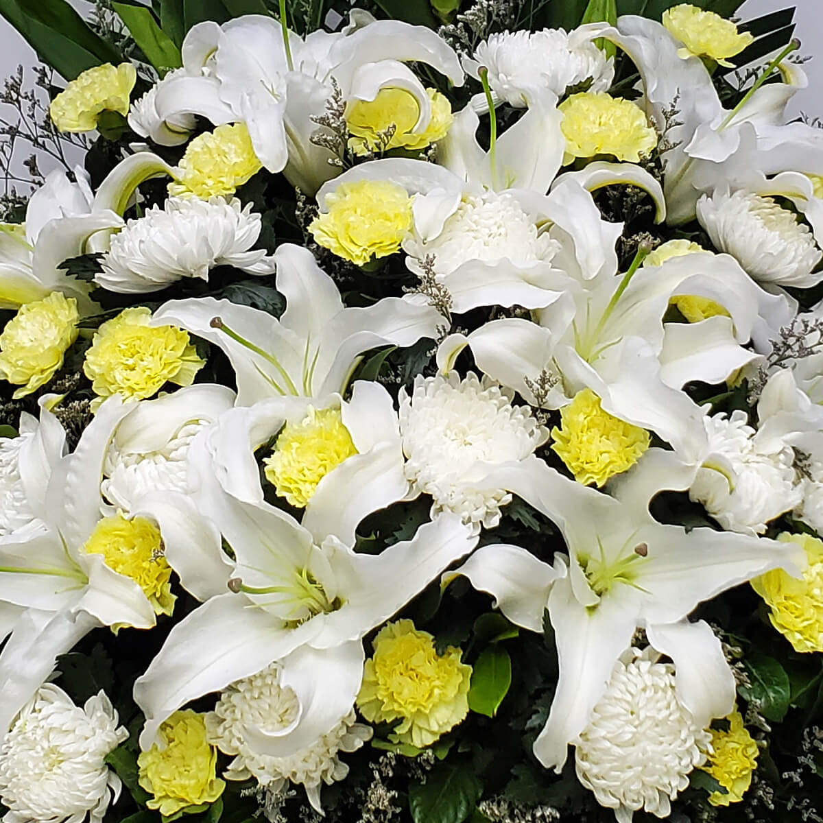 Layered floral arrangement featuring white lilies, pale yellow carnations, and white button chrysanthemums, complemented by dark foliage and filler greens - 層次花藝設計，以白百合、淡黃康乃馨及白色乒乓菊為主，配深綠葉與配草點綴