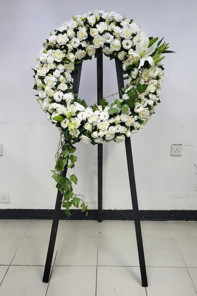 Complete wreath with white lilies, roses, lisianthus, carnations, yellow-centered chamomile flowers and cascading ivy, arranged on a black tripod stand - 白百合、玫瑰、洋桔梗、康乃馨、黃芯小白菊及垂藤綠葉圓形花圈配黑色三腳架展示