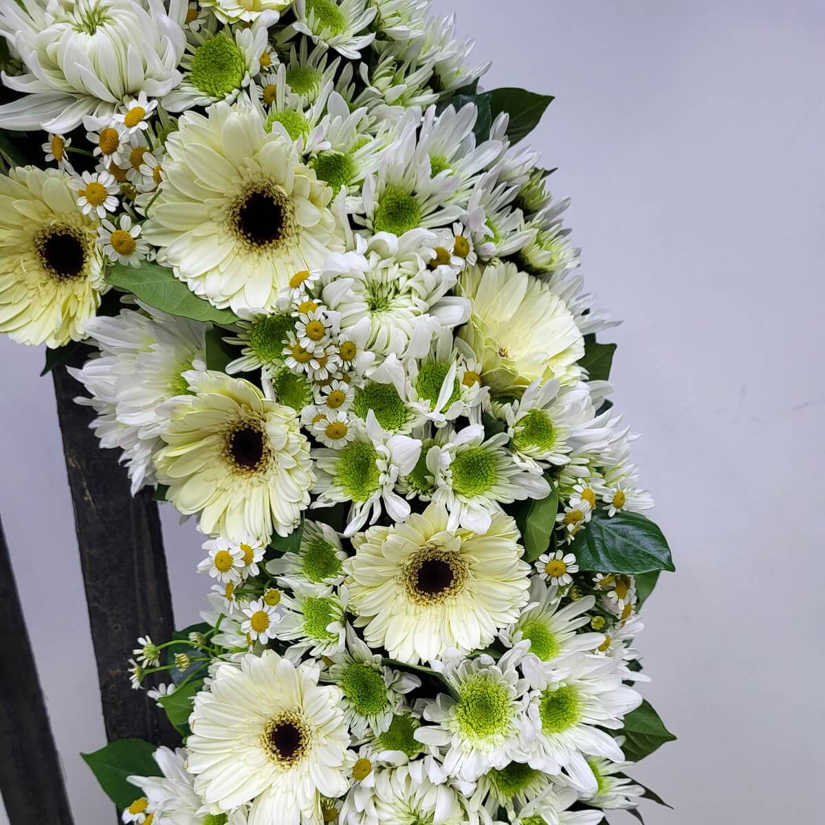 Close-up showing pale yellow gerberas, green-centered white chrysanthemums, small chamomile flowers with yellow centers, and leafy greenery - 淡黃色太陽菊、綠芯白色菊花、小白菊及鮮綠葉片局部花圈特寫畫面