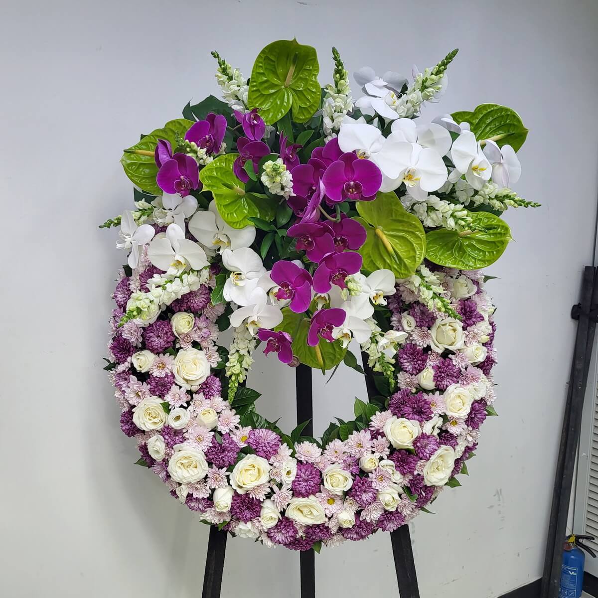 Elegant sympathy wreath adorned with white roses, lilac chrysanthemums, and cascading purple and white orchids.
白玫瑰、淡紫菊與層層蝴蝶蘭點綴的悼念花圈，展現優雅與哀思。