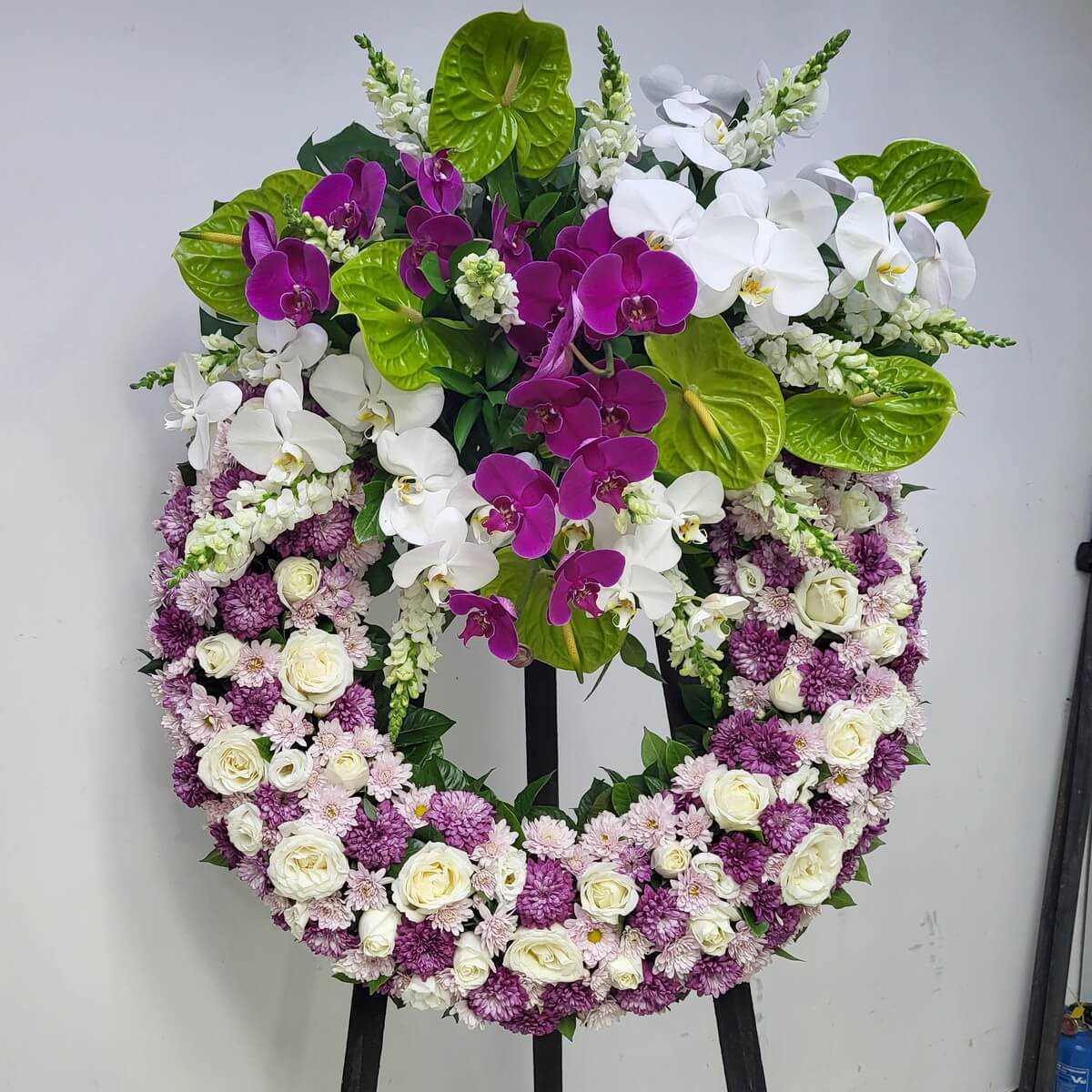 Elegant sympathy wreath adorned with white roses, lilac chrysanthemums, and cascading purple and white orchids.
白玫瑰、淡紫菊與層層蝴蝶蘭點綴的悼念花圈，展現優雅與哀思。