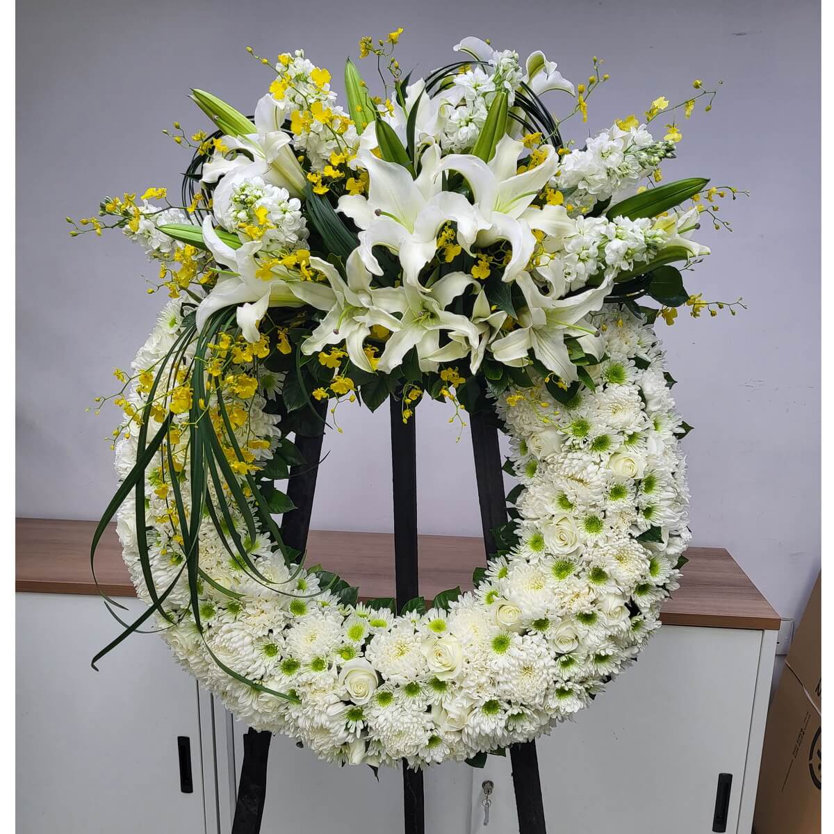 Elegant funeral wreath made with white lilies, chrysanthemums, roses, and yellow oncidium — symbolizing purity, grief, and remembrance.
喪禮花圈由白百合、菊花、玫瑰及黃小蘭組成，典雅莊重，象徵純潔、哀悼與追思之情。