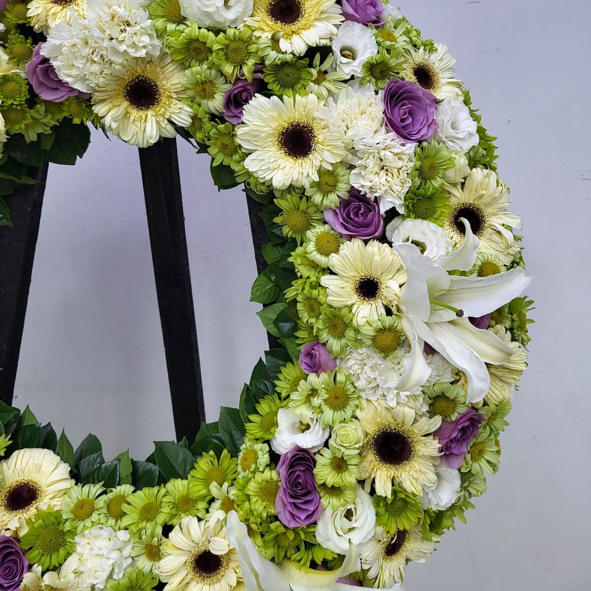Zoomed-in view of a standing funeral wreath arranged with white gerbera, green button chrysanthemums, purple roses, white lisianthus, white lilies and green foliage, original photo
白色非洲菊、綠色菊花、紫玫瑰、洋桔梗、百合及綠葉白事花圈近鏡原圖