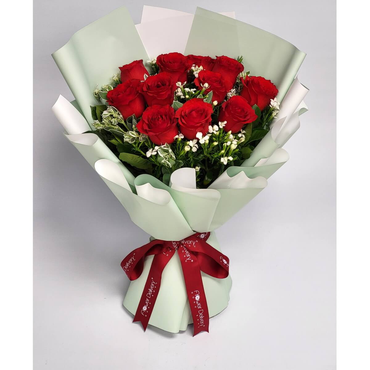 Hand-tied bouquet featuring red roses, white filler flowers, and mixed greenery wrapped in mint green 紅玫瑰搭配白色碎花與綠葉，手綁設計使用薄荷綠與白色包裝紙，綁以酒紅色絲帶，對比鮮明。