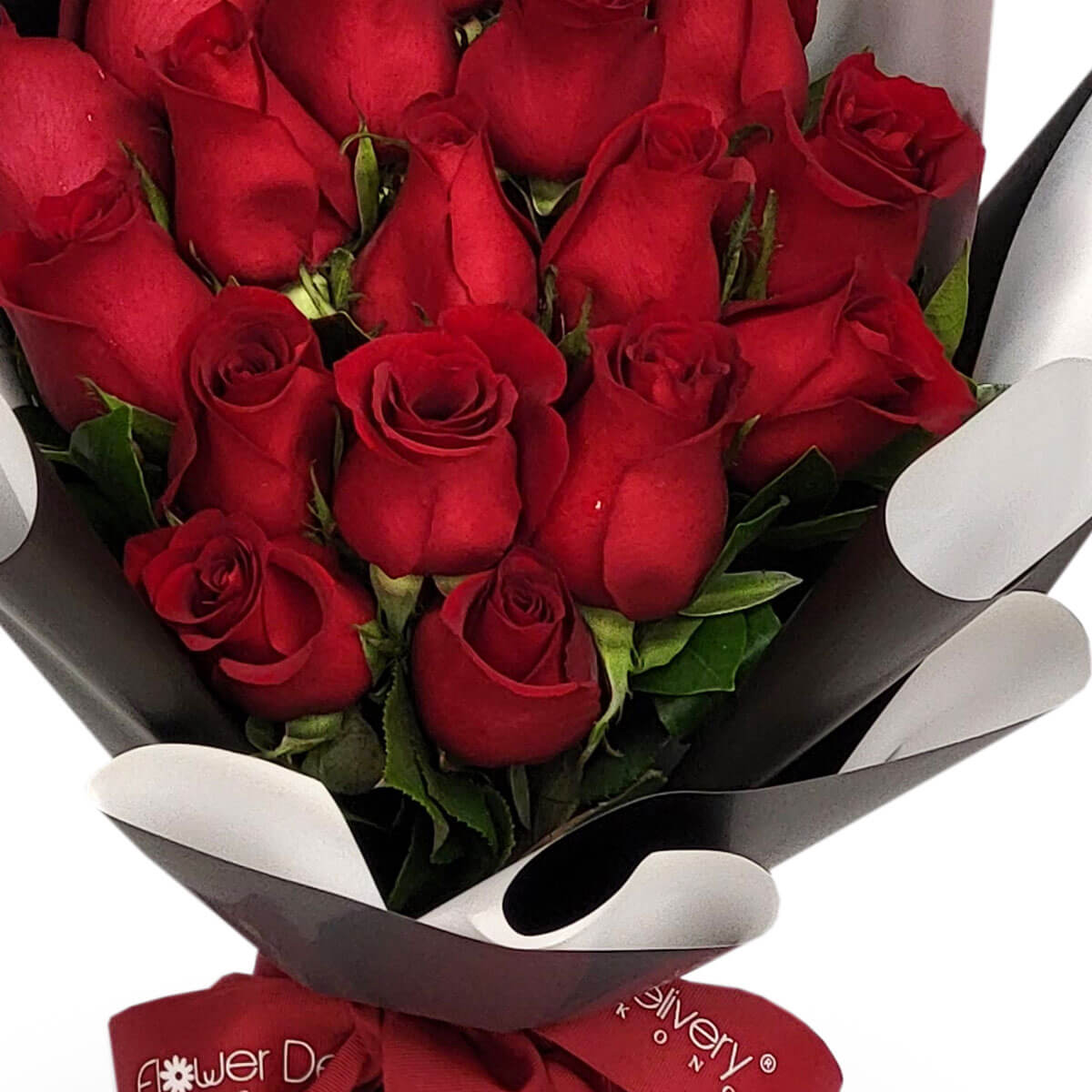 A romantic bouquet of vibrant red roses nestled in green leaves, elegantly wrapped in black and white paper – 浪漫紅玫瑰搭配綠葉，優雅黑白紙包裝