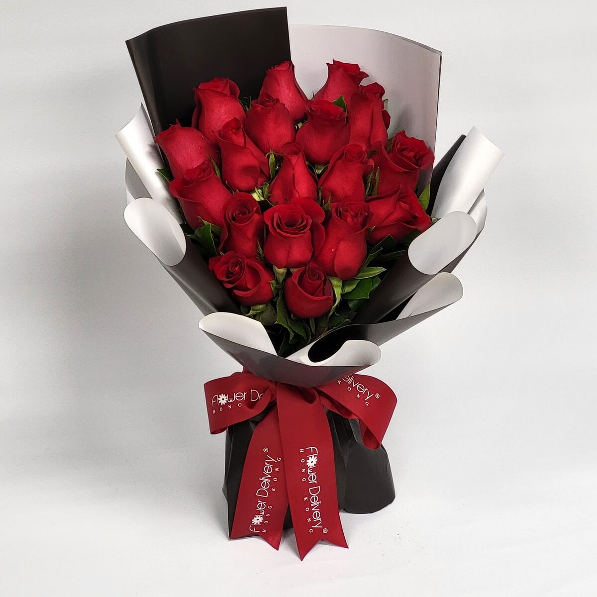 Hand-tied bouquet featuring red roses and greenery in black and white wrap 紅玫瑰花束搭配綠葉設計，手綁風格配以黑白色包裝紙，紅色絲帶束口，造型鮮明大氣。