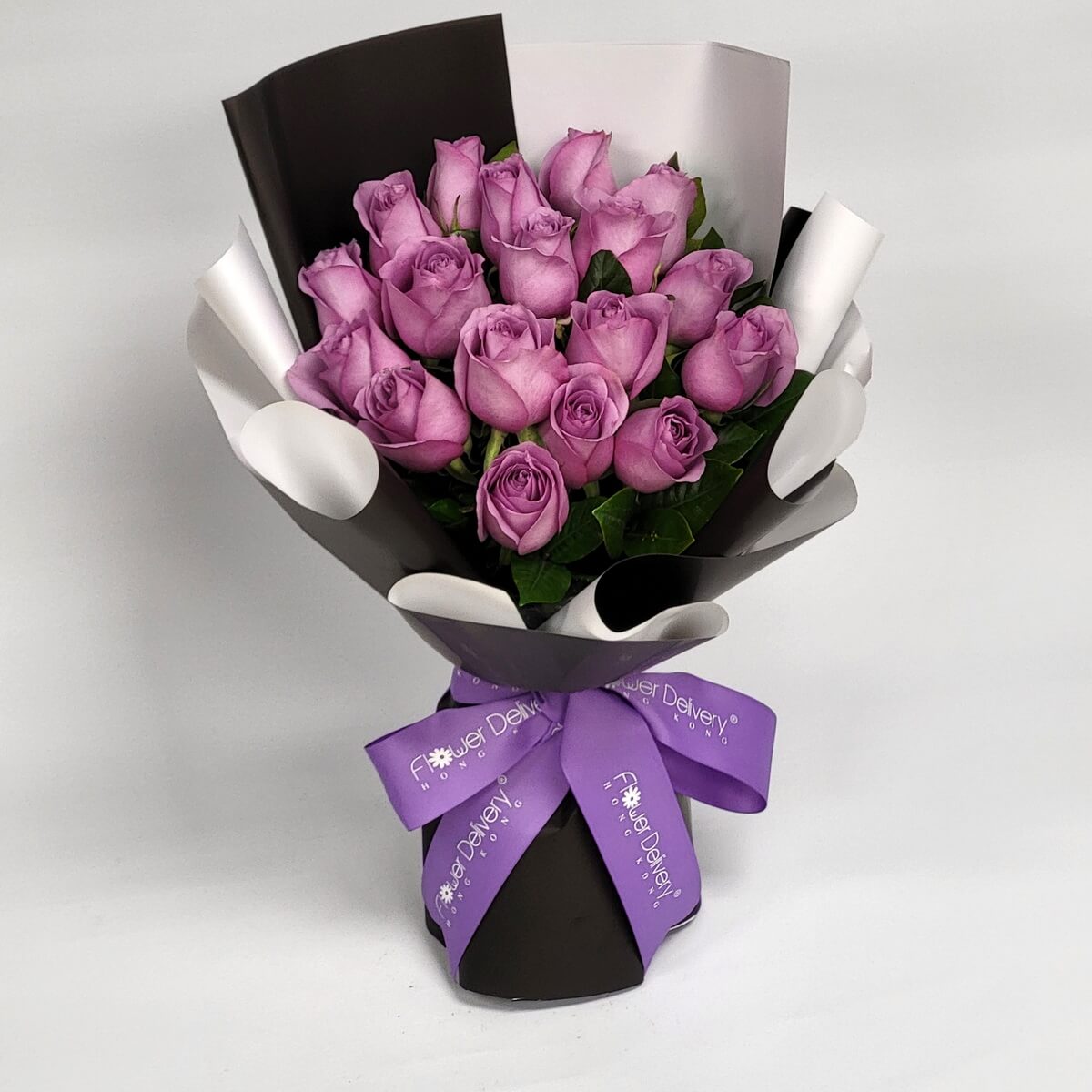 Hand-tied bouquet featuring lavender roses and greenery in black and white wrap 淺紫玫瑰花束配搭綠葉，手綁設計使用黑白色包裝紙，紫色絲帶點綴，色調對比鮮明。
