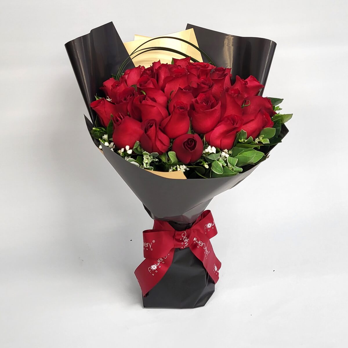 Hand-tied bouquet featuring red roses, white fillers, and foliage wrapped in black and gold paper 鮮紅玫瑰緊密排列，搭配白色襯花及綠葉設計，包以黑色與金色包裝紙，紅絲帶束口。