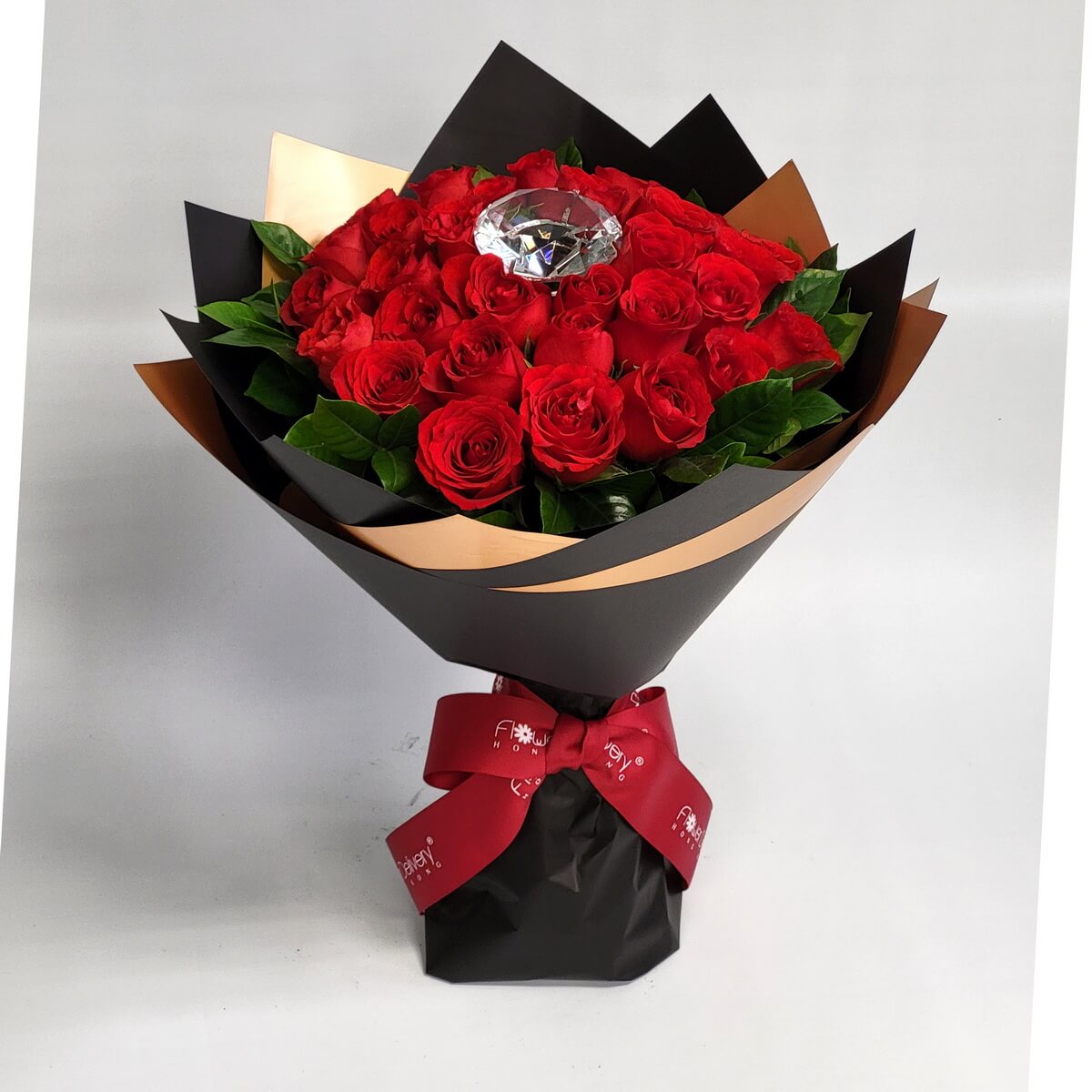 Hand-tied bouquet of red roses and greenery, featuring a faux diamond accent 紅玫瑰搭配綠葉設計，中央鑲嵌仿水晶鑽石作亮點，黑色與銅色包裝紙包裹，紅色絲帶束口，手綁造型大方奪目。