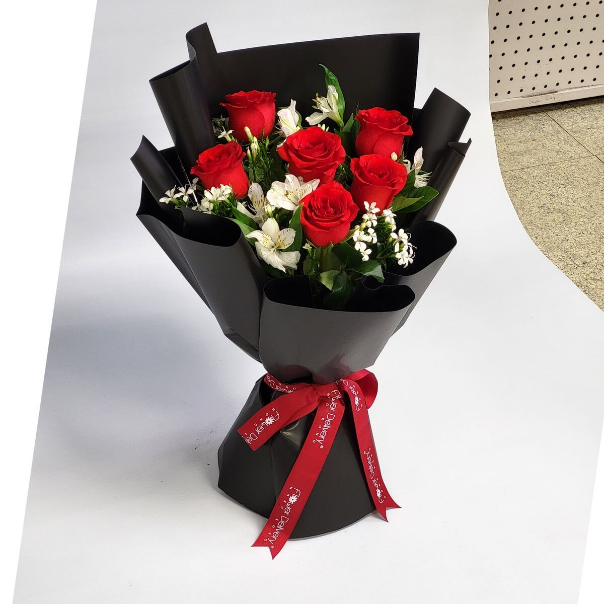 Hand-tied bouquet featuring red roses, white alstroemeria, and filler flowers wrapped in black 紅玫瑰、白百合草及白色碎花組合設計，手綁花束配黑色包裝紙及紅色絲帶，對比鮮明。