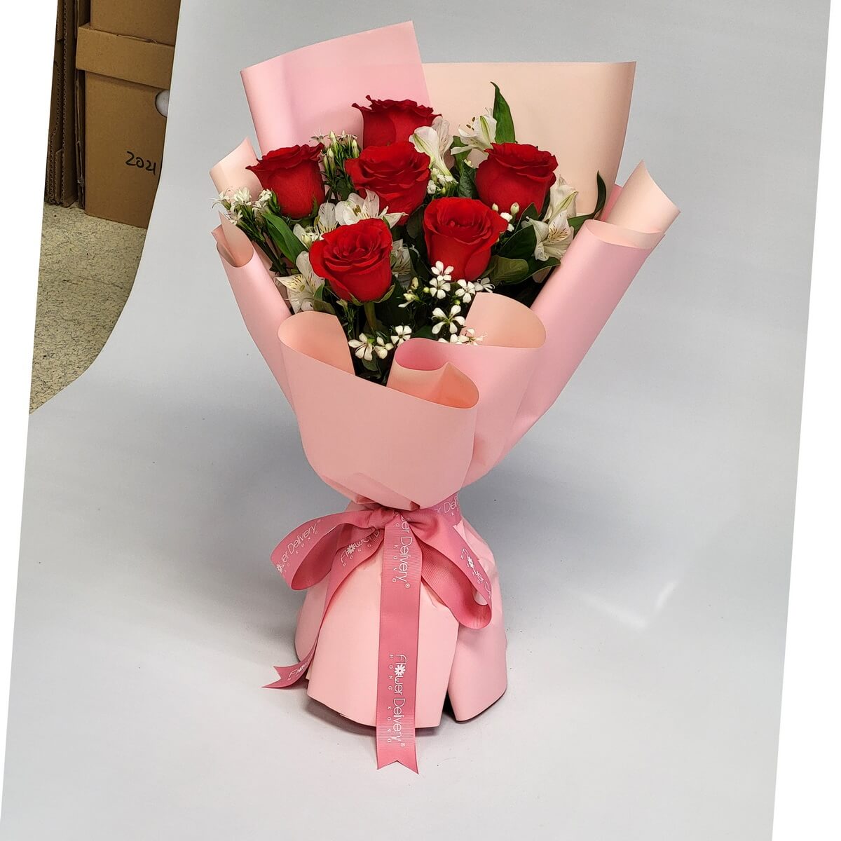 Hand-tied bouquet featuring red roses, white alstroemeria, and filler flowers 紅玫瑰、白色百合草及白色碎花組合手綁花束，粉紅色包裝紙配同色絲帶束口，清新雅緻設計。