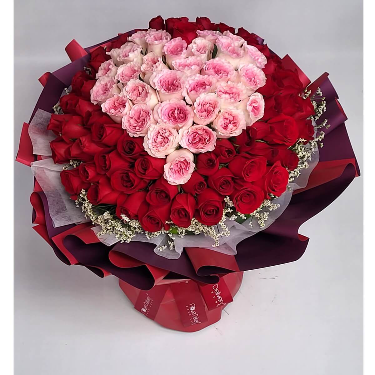 Large round bouquet with pink garden roses in the center and red roses around, accented with white fillers 大型圓形手綁花束設計，粉紅玫瑰為中心主花，外圍搭配鮮紅玫瑰及白色碎花，層次分明。