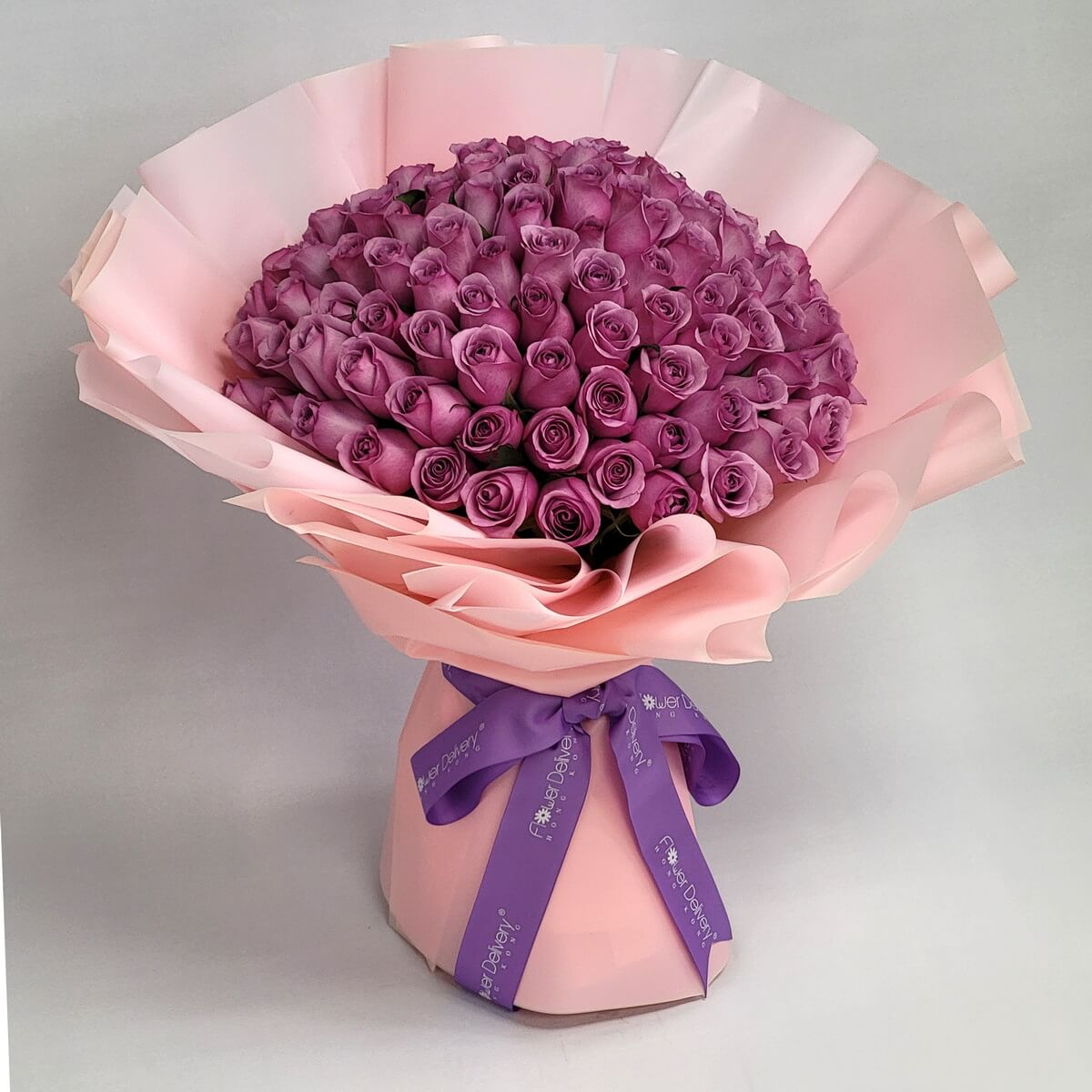 Original full view of dome-shaped purple rose bouquet featuring tightly packed blooms, wrapped in soft layered pink paper and finished with a decorative purple ribbon 圓頂紫玫瑰花束，花朵緊密排列，配柔粉多層包裝紙及紫色絲帶點綴