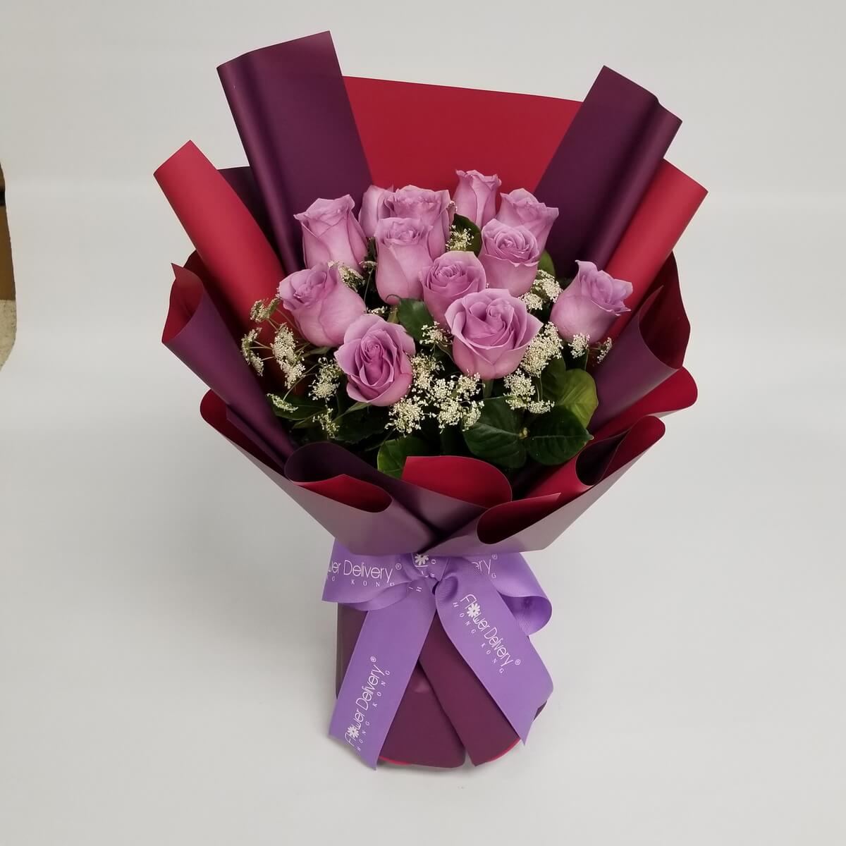 Hand-tied bouquet with lavender roses, white filler flowers, and foliage in rich red and plum wrapping 淺紫玫瑰襯以白色碎花與綠葉，採用深紅與紫色包裝紙設計，綁以紫色絲帶束口。