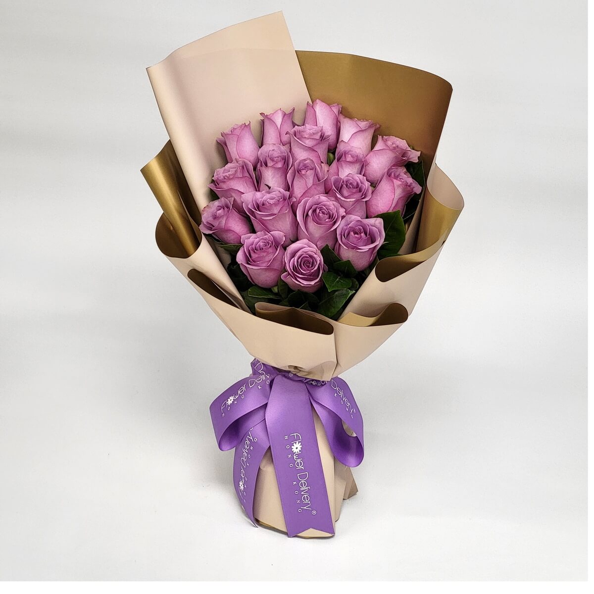 Hand-tied bouquet featuring lavender roses and green foliage in champagne and gold wrap 淺紫玫瑰配綠葉，手綁設計，採用香檳色與金色包裝紙，綁以紫色絲帶。
