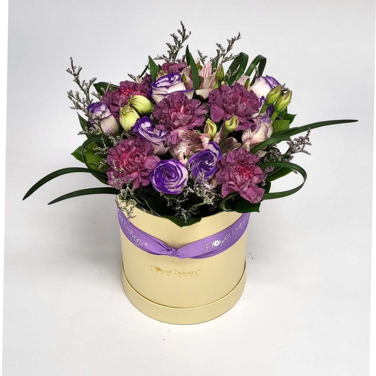 Round cream hat box with purple lisianthus, mauve carnations, and pale alstroemeria 淺奶黃花盒內配搭紫色洋桔梗、粉紫康乃馨及淡粉色百合草花材，搭配綠葉。