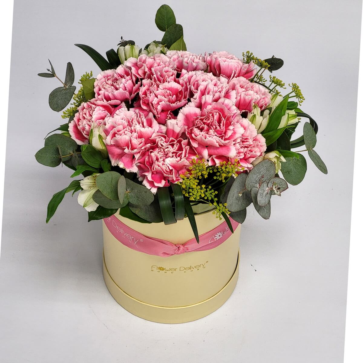 Round box arrangement of pink-edged carnations with white alstroemeria, eucalyptus leaves, and assorted greenery 粉邊康乃馨、白色六出花與尤加利葉混合設計花盒，米色圓形花盒配粉紅絲帶，造型清新自然。