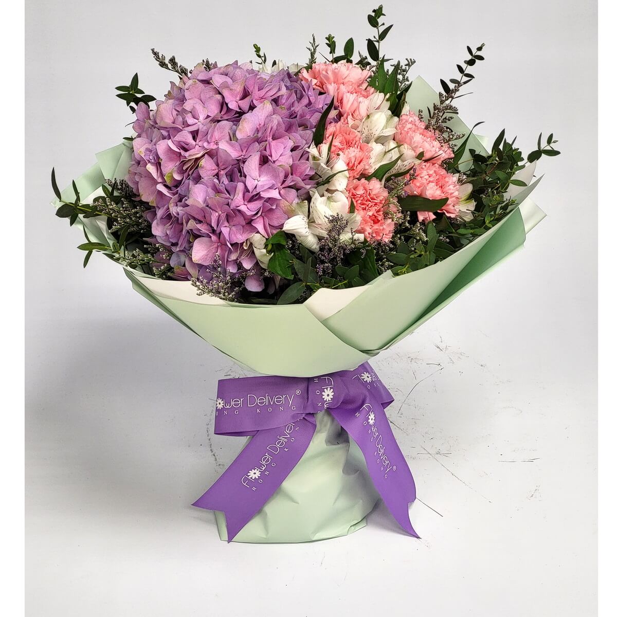 Full bouquet featuring purple hydrangeas, pink carnations, and white alstroemeria, wrapped in green paper 紫繡球花、粉紅康乃馨及白色六出花組成花束，以淡綠包裝紙包裹，配搭紫色絲帶，清新雅緻。