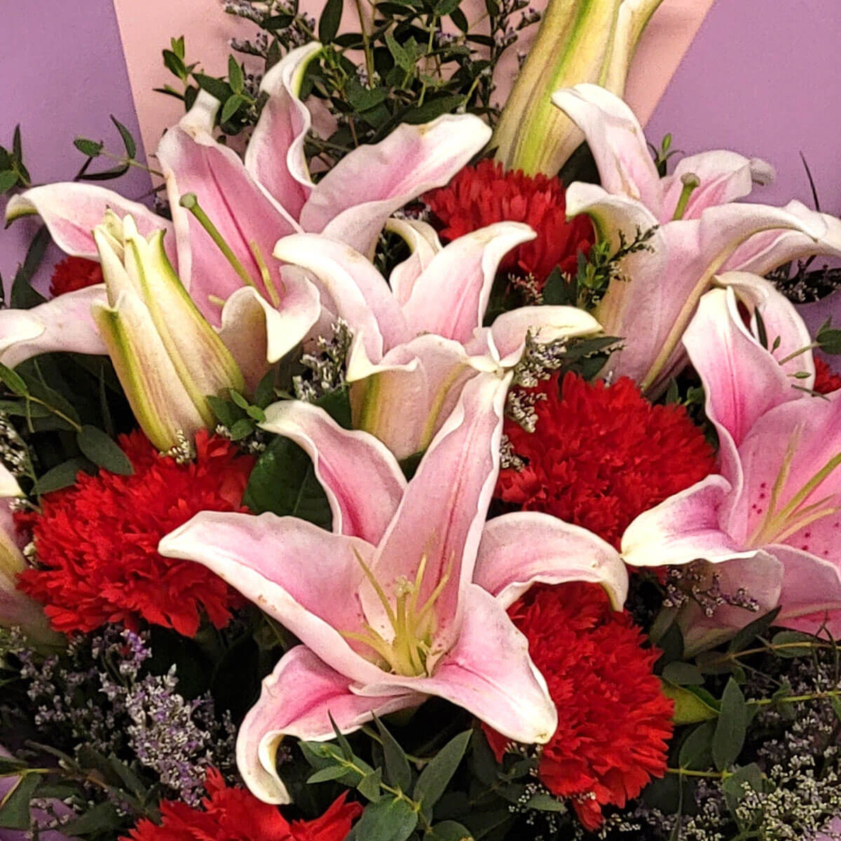 Pink lilies bloom alongside red carnations 粉色香水百合與紅色康乃馨交織成美麗畫面，點綴紫花與綠葉，展現高貴與熱情的完美結合。